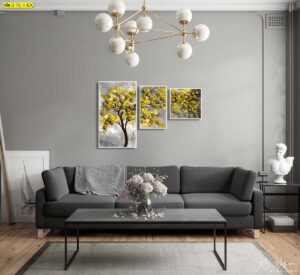 ห้องนั่งเล่นสไตล์โมเดิร์นโทนเทา‑ดำ ตกแต่งด้วยภาพชุดต้นไม้ดอกสีทองสามชิ้น เหนือโซฟาทรงยาว สีทองตัดพื้นหลังเทาให้ความหรู เรียบ และเป็นจุดโฟกัสของผนัง